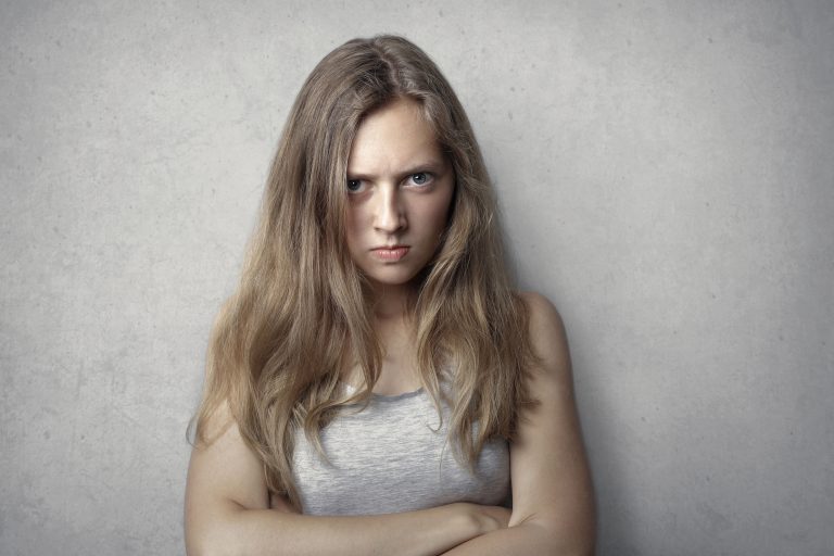 Woman with crossed arms looking unhappy against a grey background